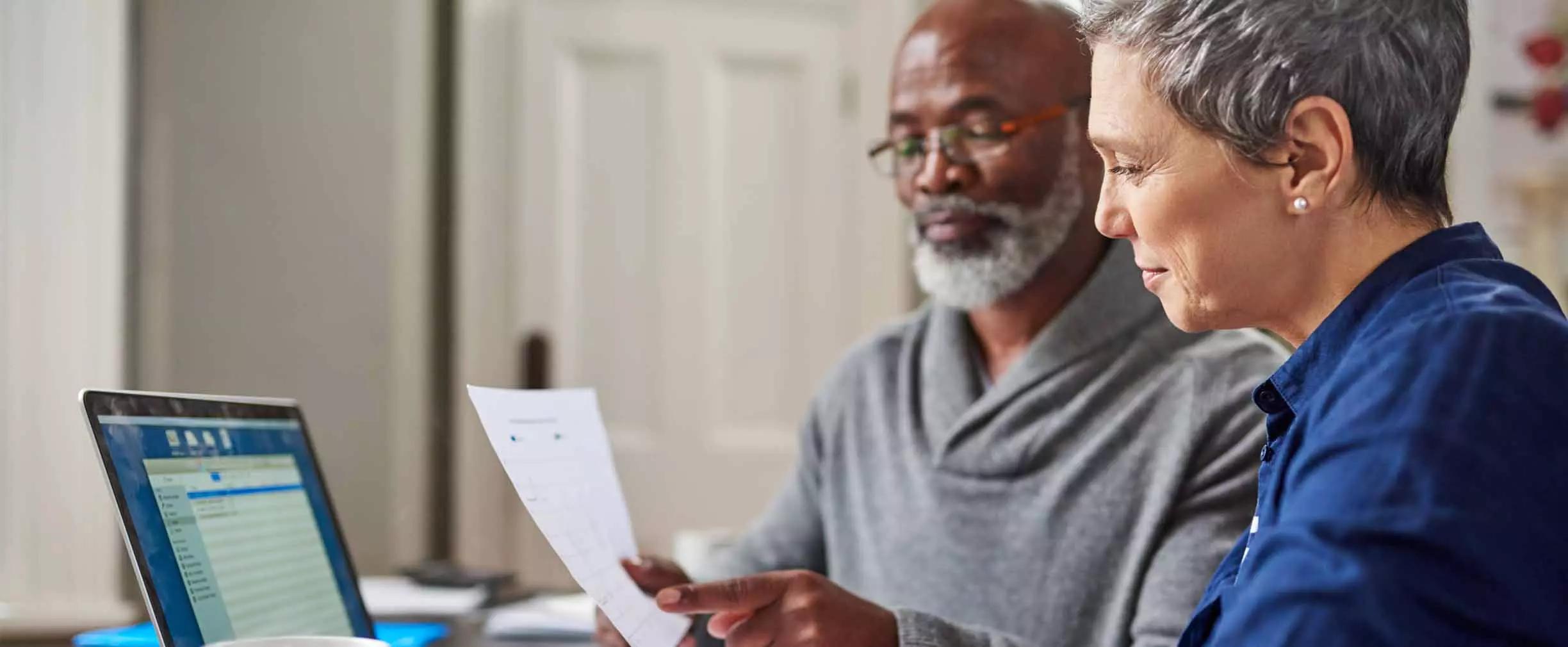 A man and a woman, seated next to each other at a table, review a document together.